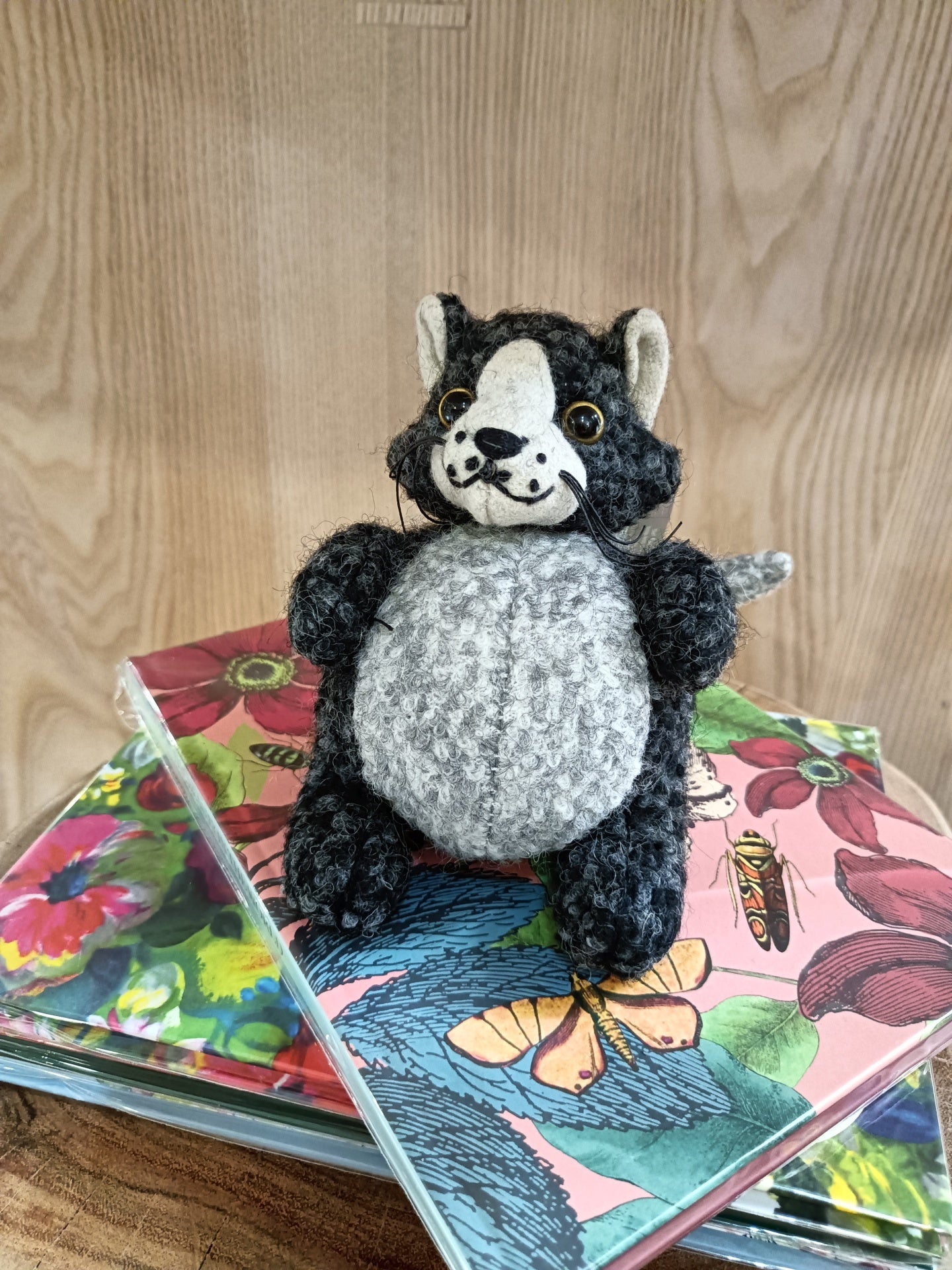 Boneco de peluche gato preto e cinzento em cima de cadernos coloridos com flores e borboletas