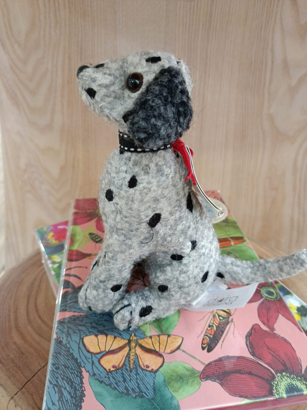 Pelúcia de cachorro cinzento com manchas pretas e orelhas escuras sobre caixa decorada.