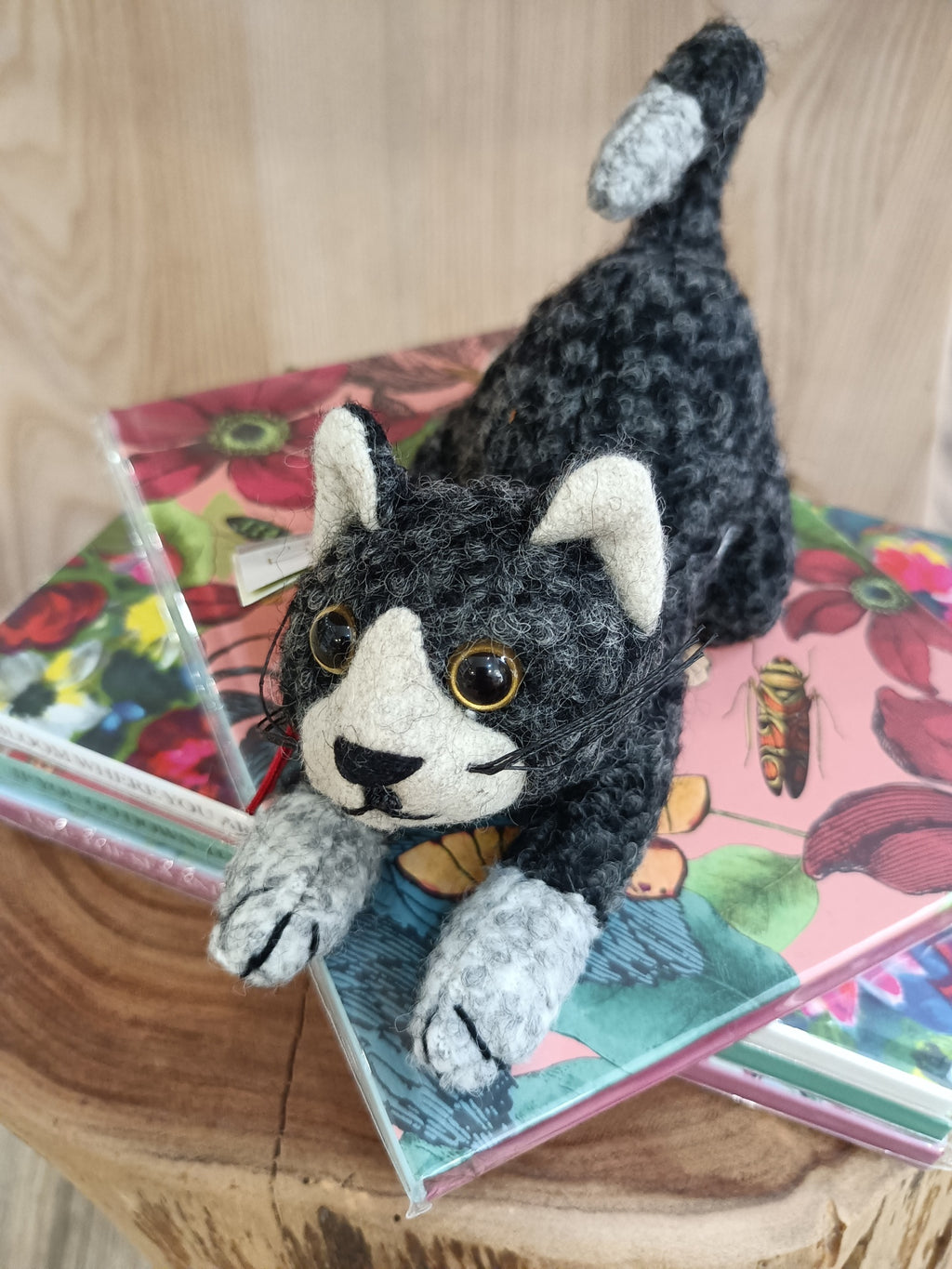 Pelúcia de gato cinza e preta em cima de livros florais sobre madeira
