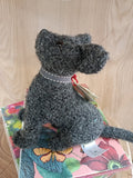 Boneco de cão cinzento de lã feltrada sentado em caixa floral colorida