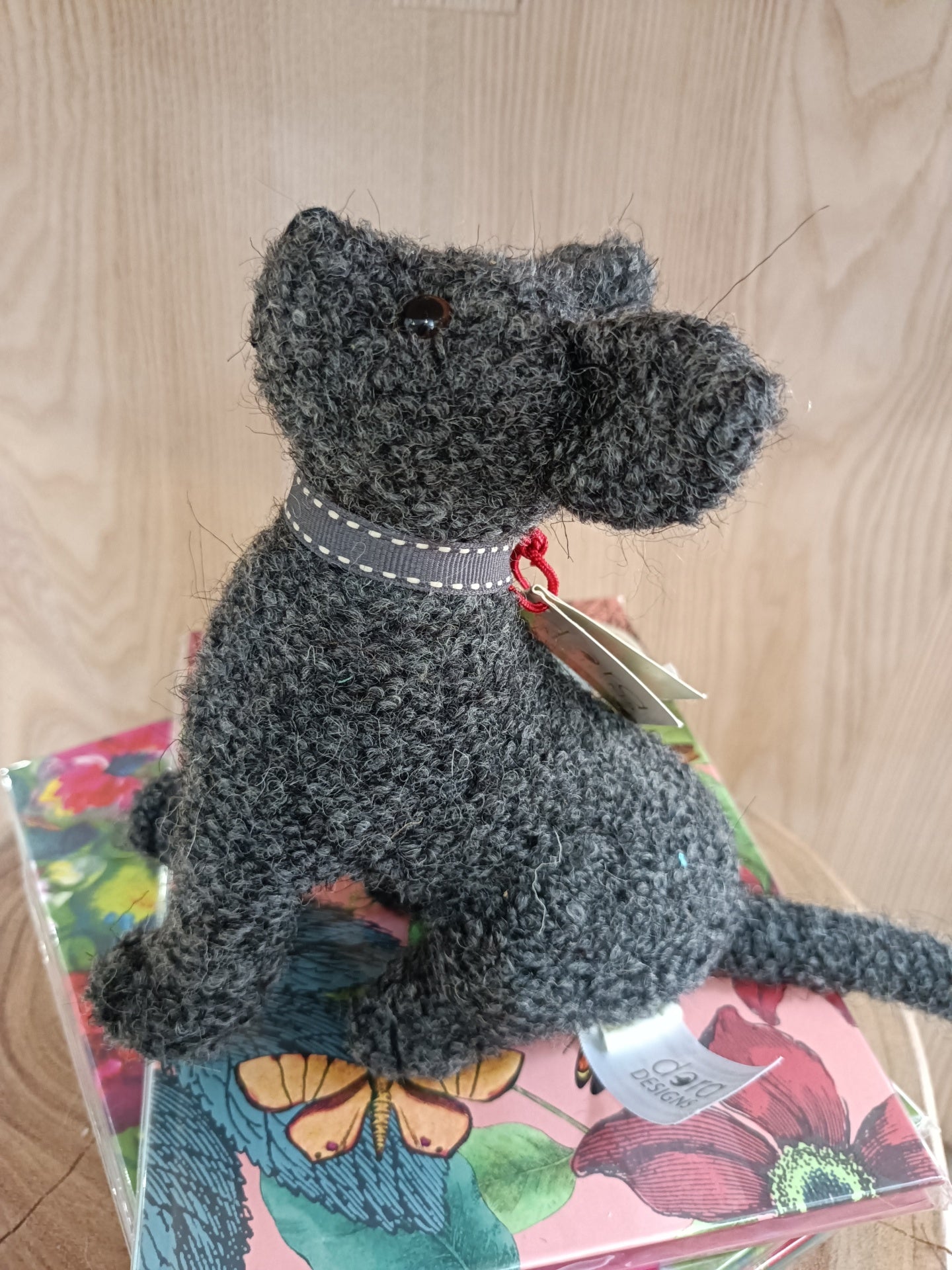 Boneco de cão cinzento de lã feltrada sentado em caixa floral colorida