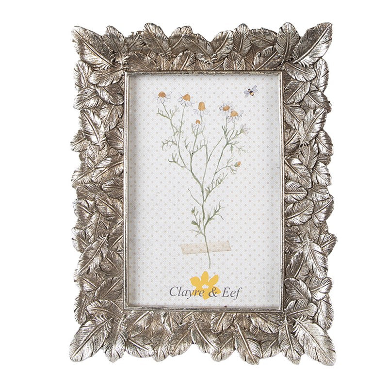 Moldura decorativa prateada com relevo de folhas e ilustração de flor interna.