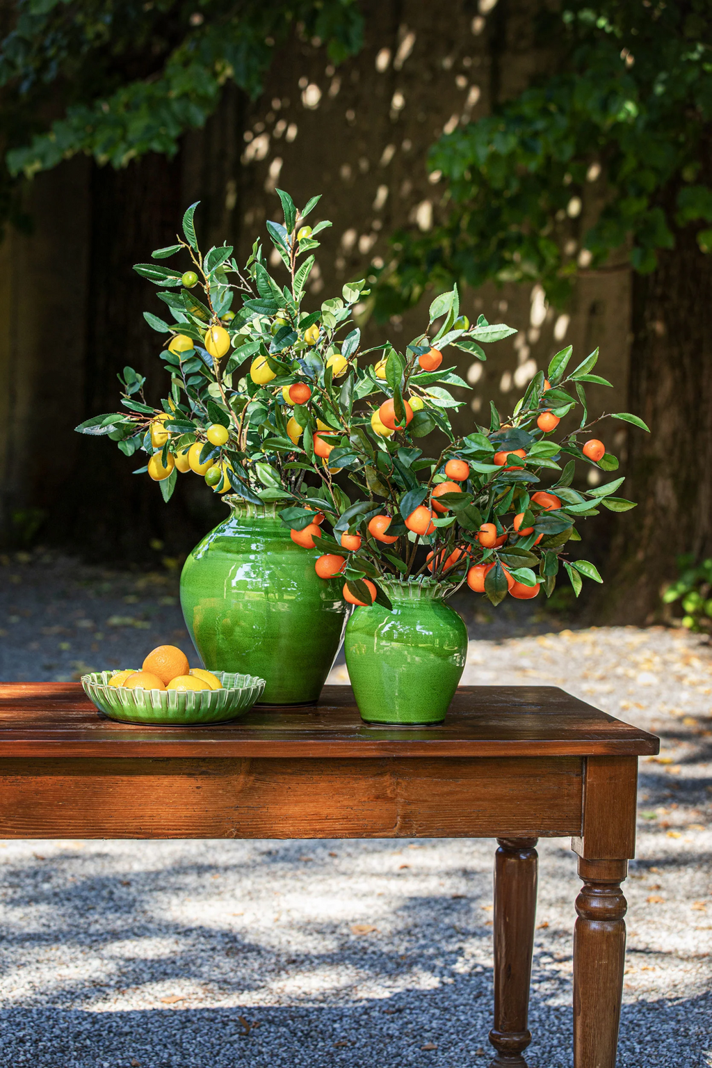 Vasos verdes com ramos de frutas e prato com citrinos na mesa de madeira ao ar livre