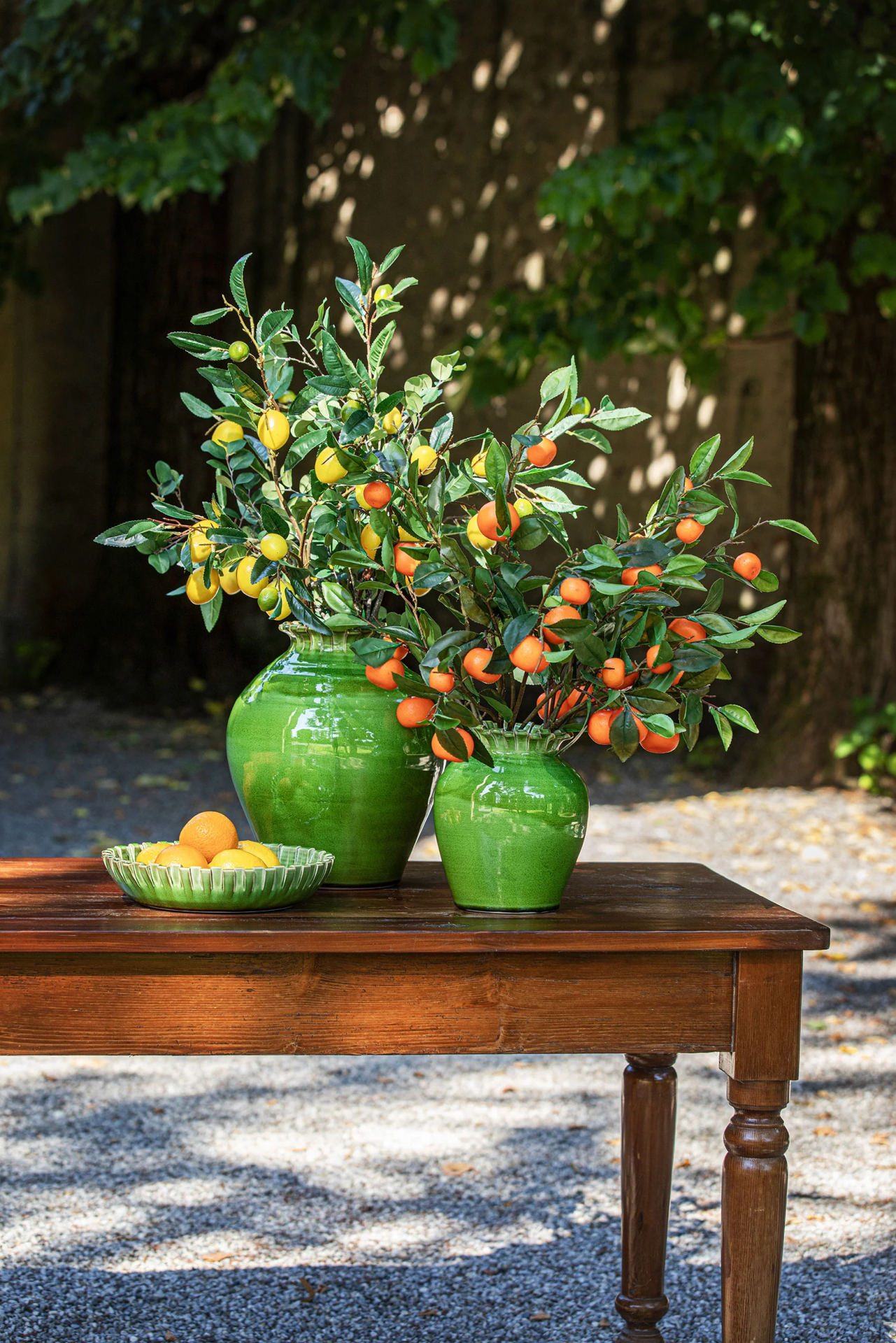 Vasos verdes com ramos de frutas e prato com citrinos na mesa de madeira ao ar livre