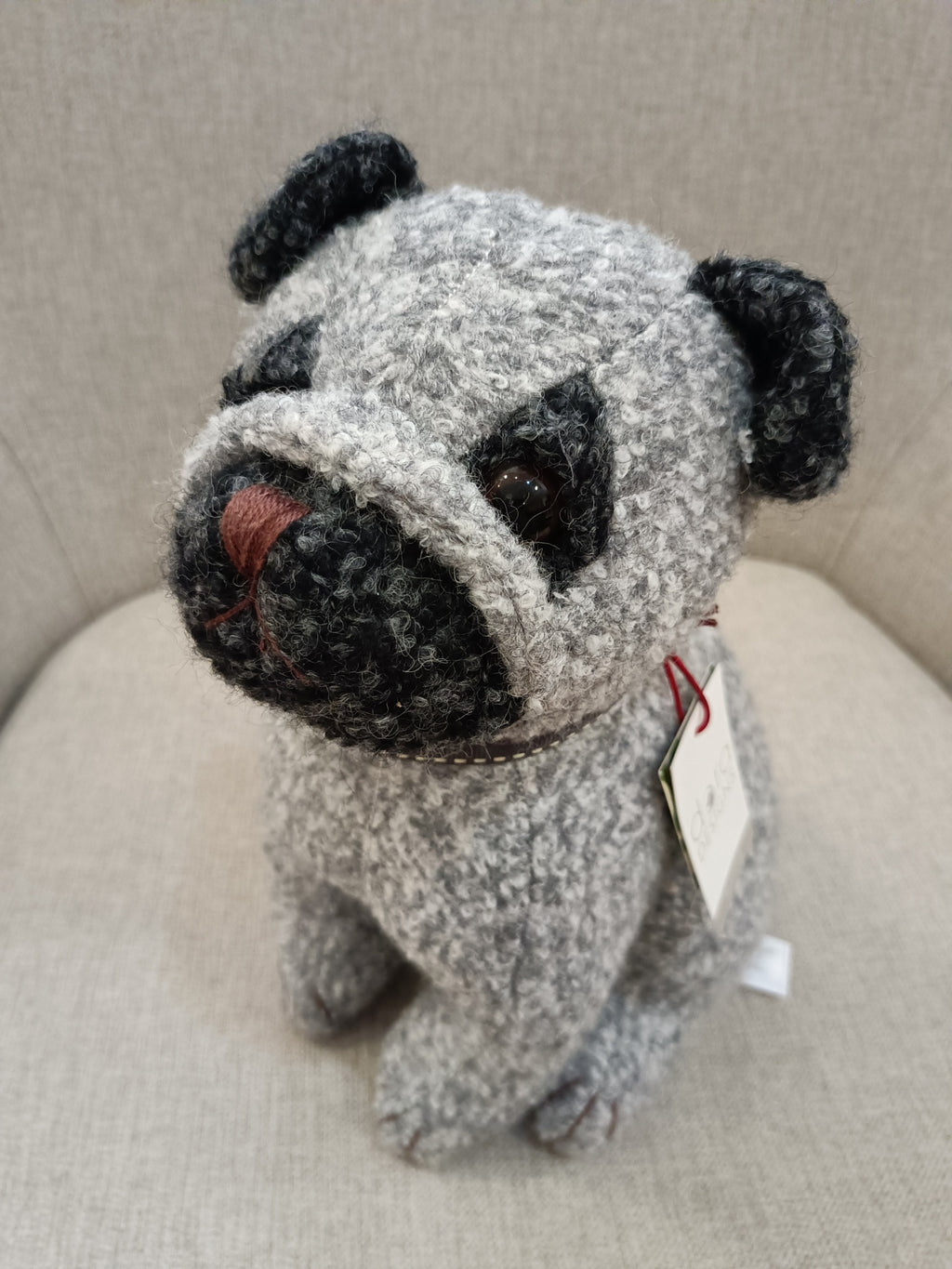 Pelúcia de cão pug cinzento e preto sentada num sofá bege