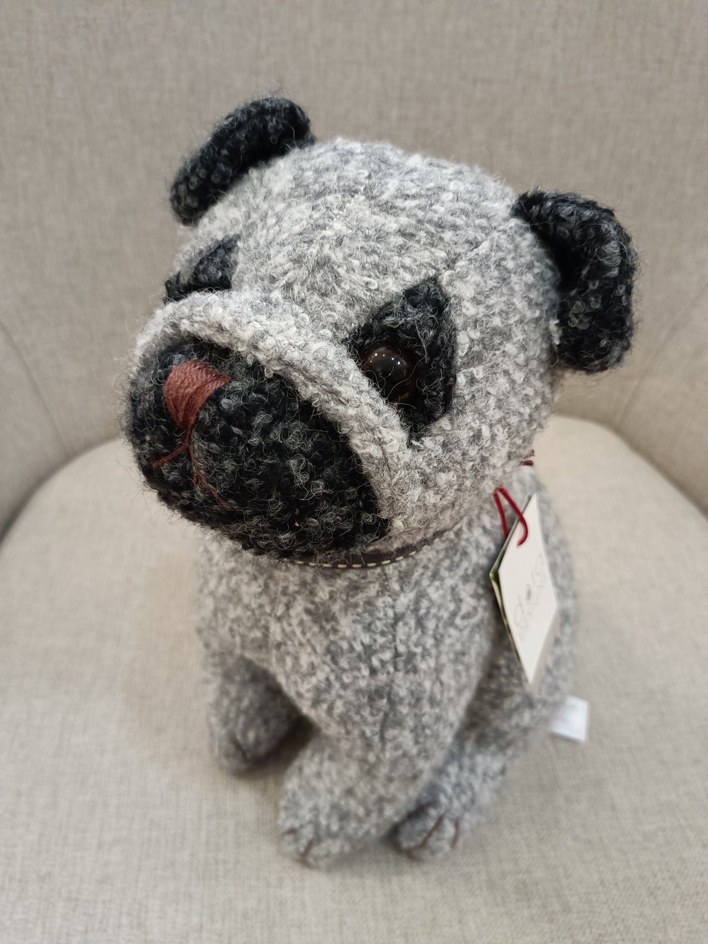 Pelúcia de cão pug cinzento e preto sentada num sofá bege
