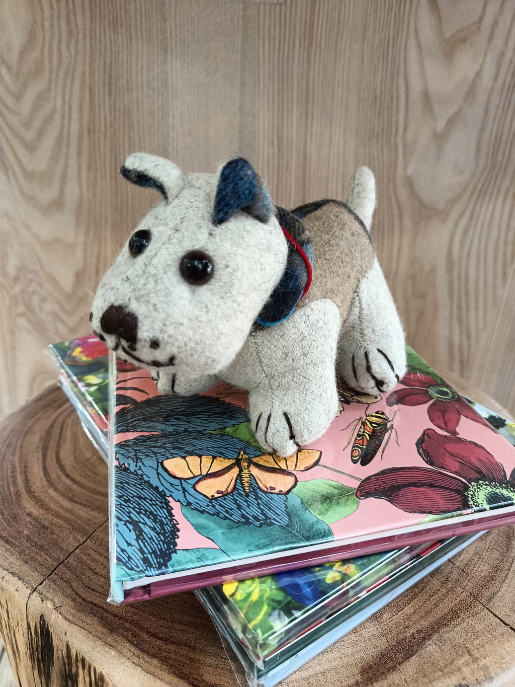 Cão de pelúcia bege e castanho sobre livros coloridos com padrão de borboletas e flores, em superfície de madeira