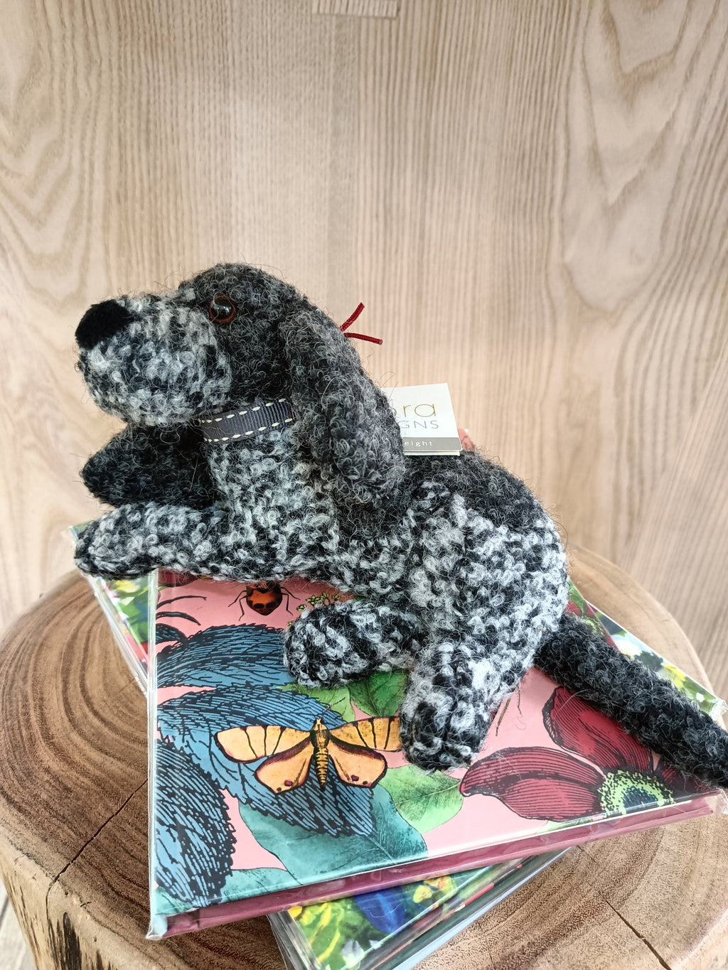 Pelúcia cão cinzento preto e branco com coleira sobre livros coloridos em mesa de madeira