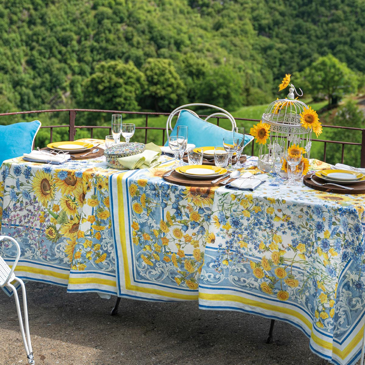 Mesa decorada com toalha estampada de girassóis, pratos, copos e gaiola com girassóis