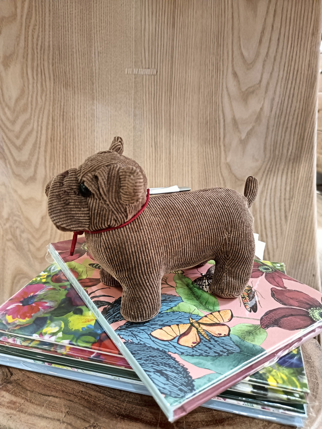 Peluche de cão castanho em tecido de veludo cotelê com coleira vermelha sobre cadernos florais