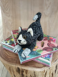 Gato de croché preto e branco sobre cadernos florais coloridos numa base de madeira