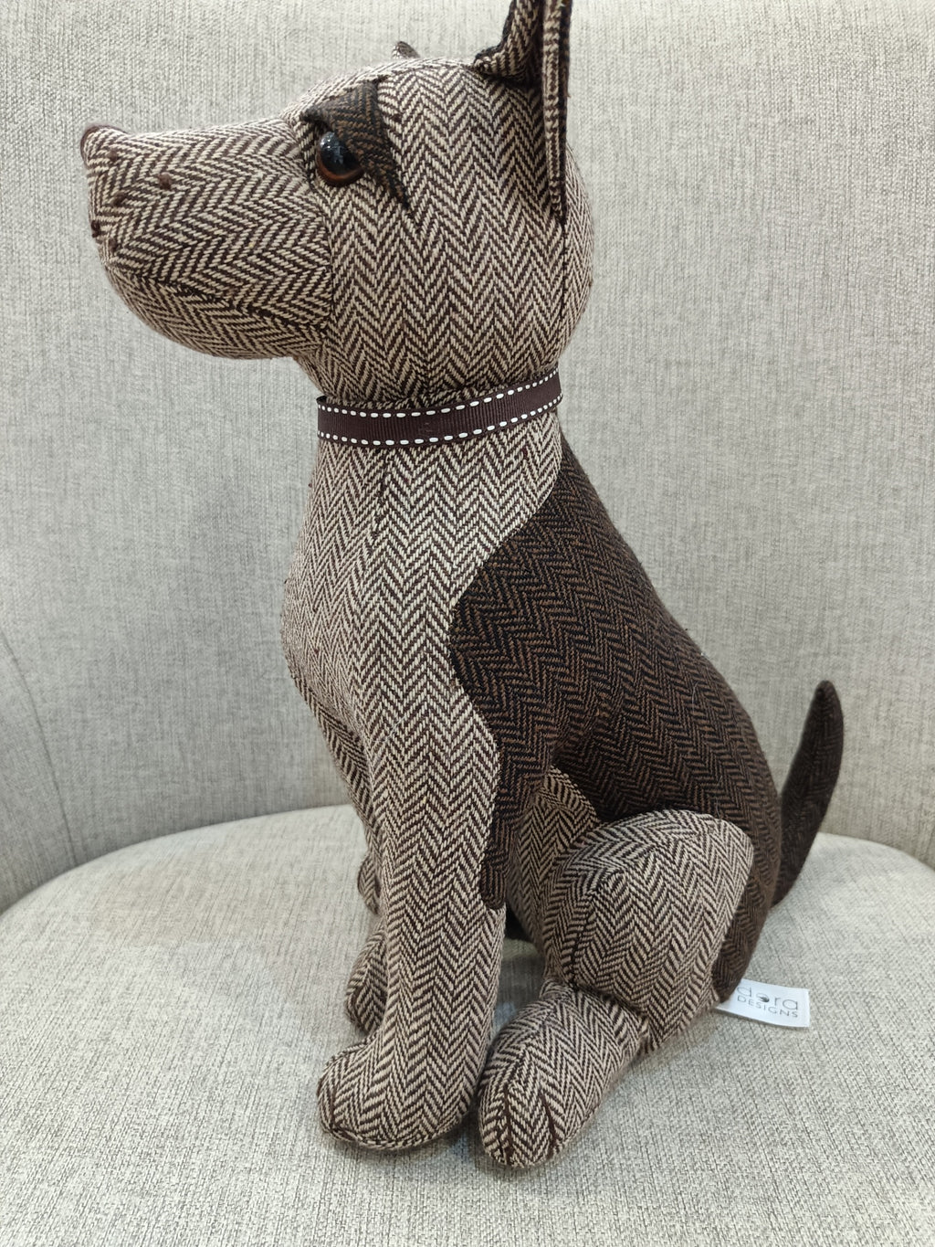 Boneco de cão de tecido castanho e bege sentado numa cadeira cinzenta clara