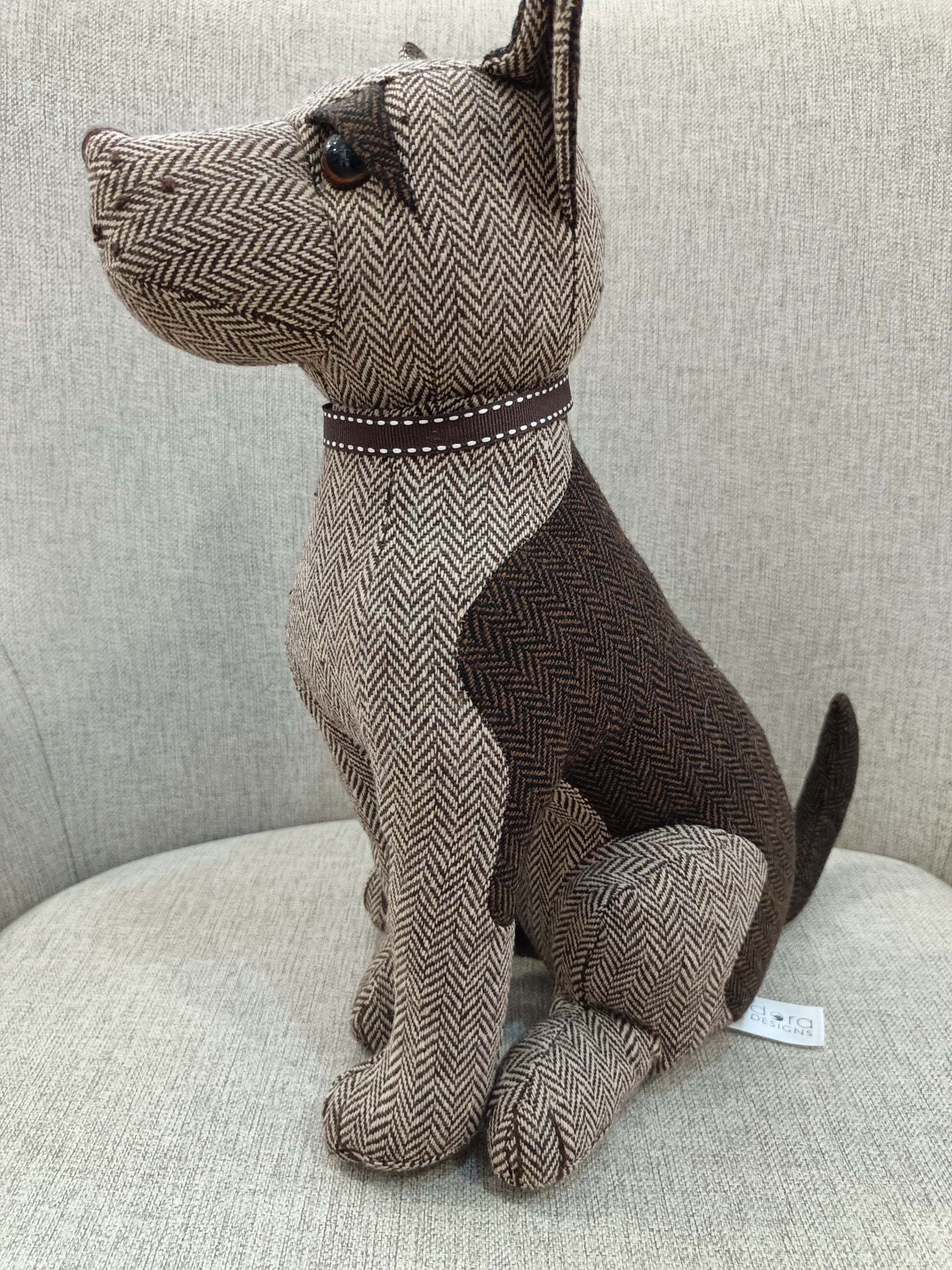 Boneco de cão de tecido castanho e bege sentado numa cadeira cinzenta clara