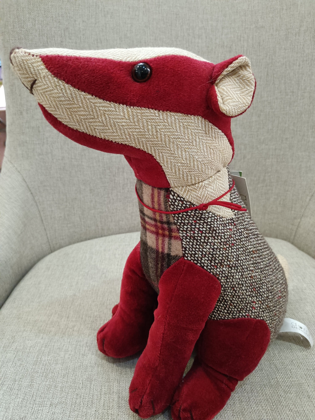 Boneco de tecido em forma de cão com vários padrões coloridos sentado numa cadeira cinza claro.
