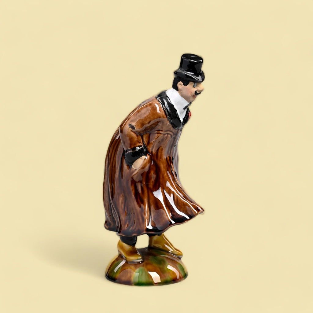 Figura decorativa cerâmica de homem com casaco castanho e chapéu preto.