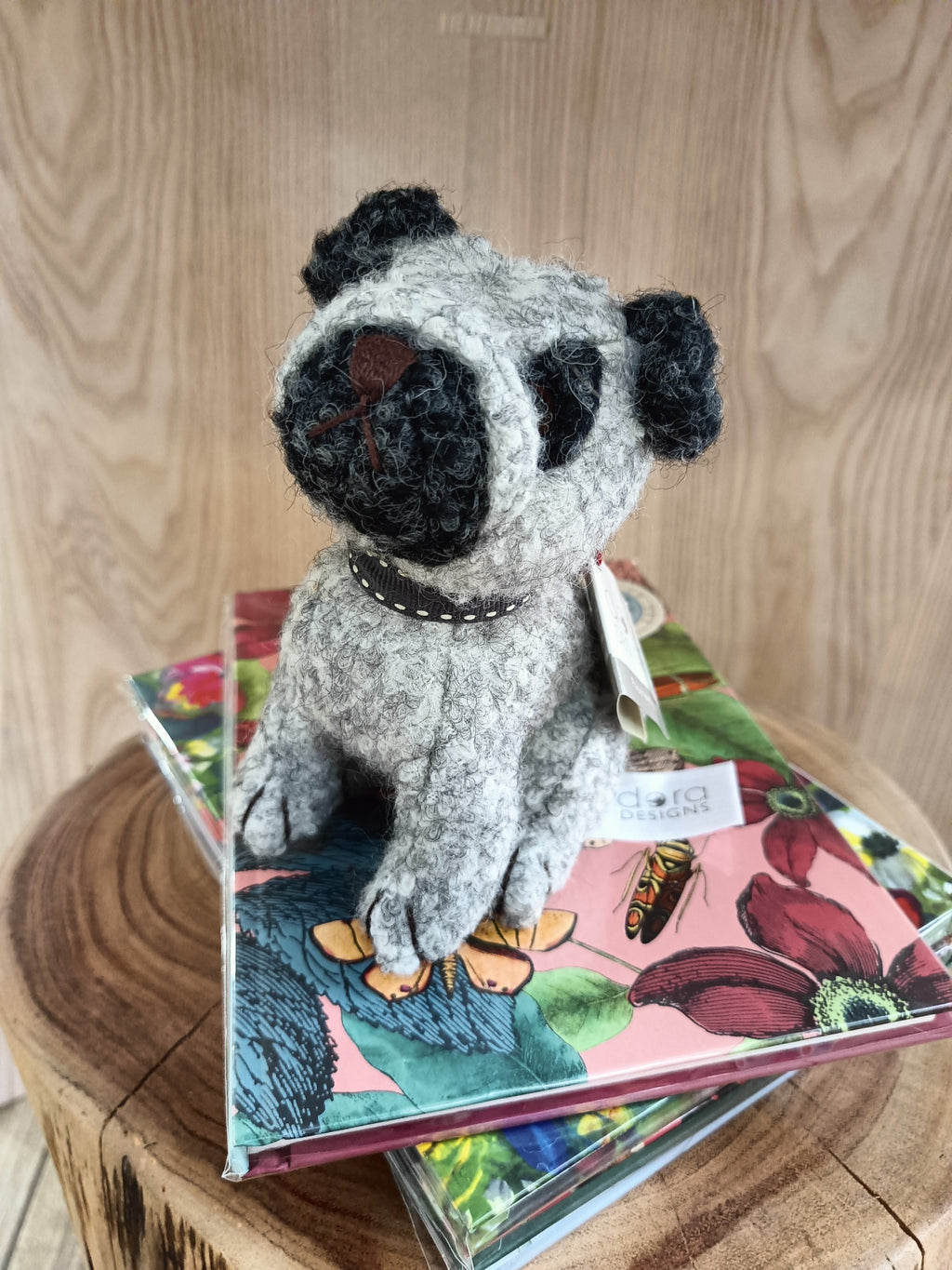 Boneco de cão de malha cinzento sobre cadernos florais em tronco de madeira