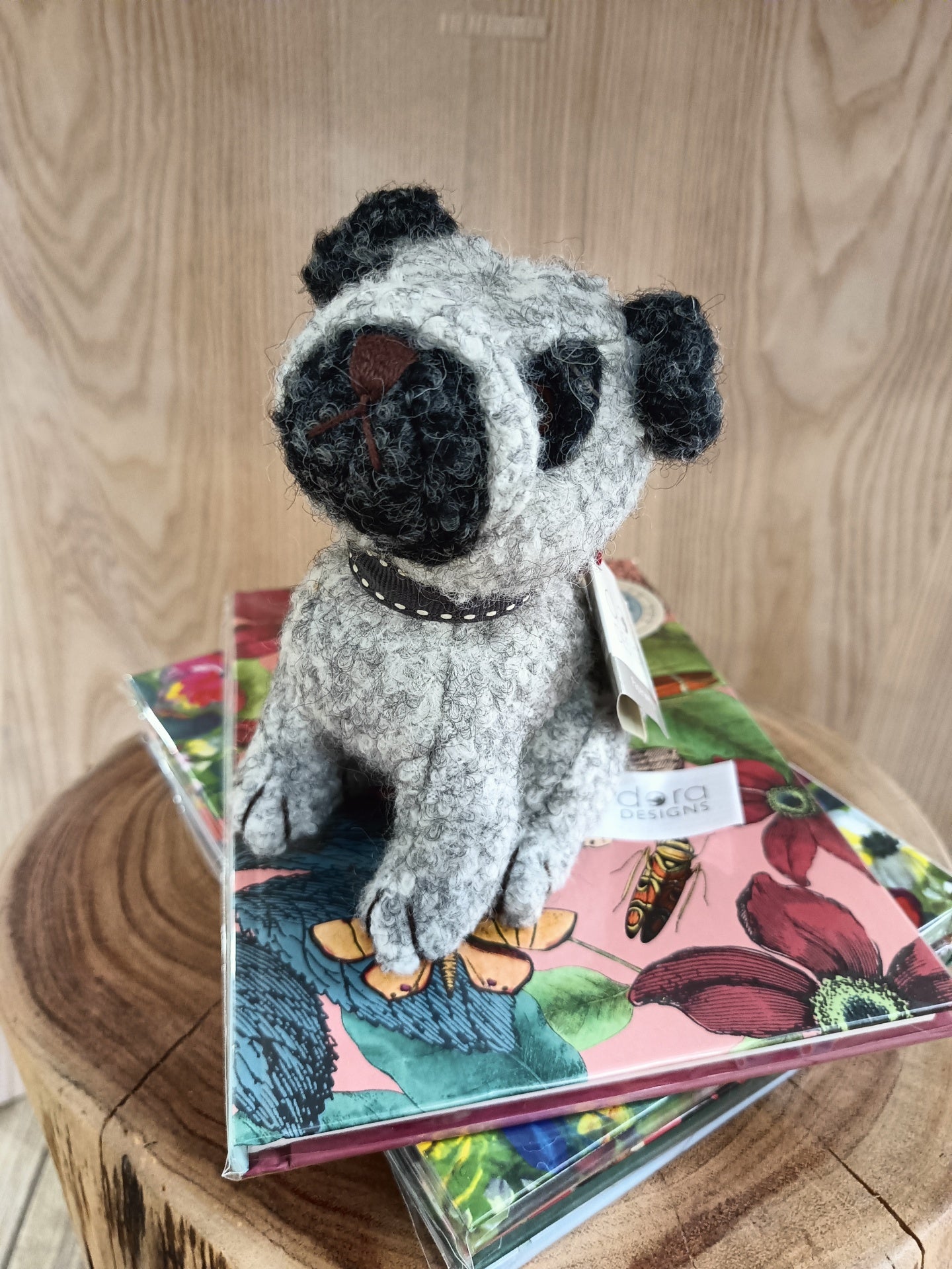 Boneco de cão de malha cinzento sobre cadernos florais em tronco de madeira