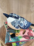 Pelúcia de pássaro com padrões florais azuis sobre livros coloridos com flores e insetos