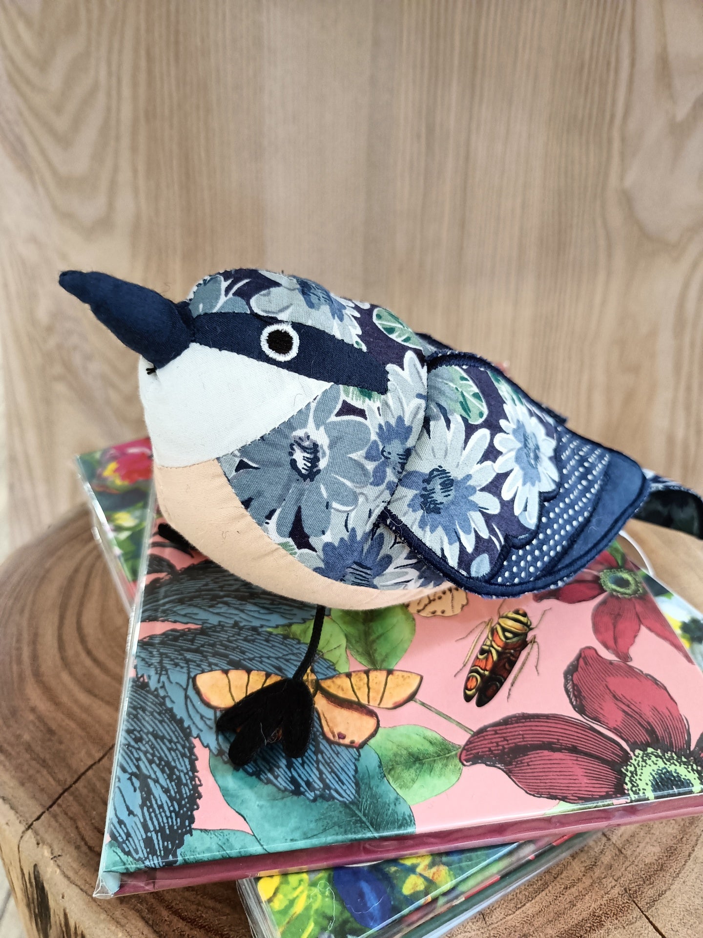 Pelúcia de pássaro com padrões florais azuis sobre livros coloridos com flores e insetos