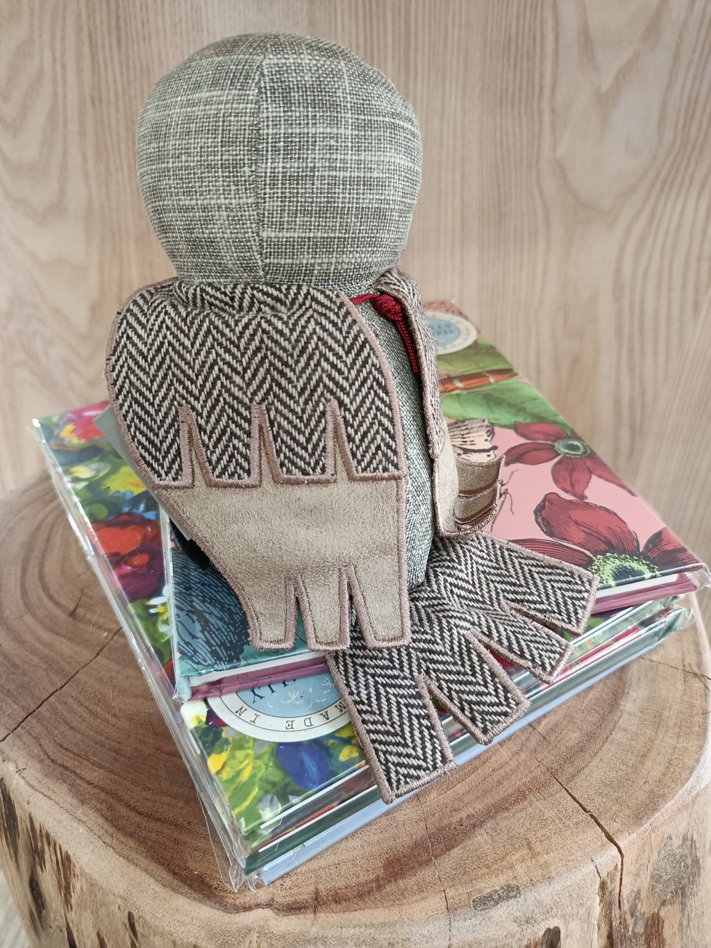 Boneco de tecido cinzento e bege sentado sobre livros coloridos numa superfície de madeira