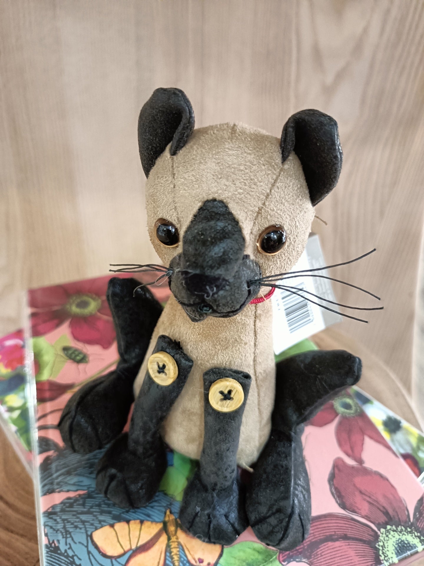 Boneco de peluche de animal bege e preto sentado em caixa floral