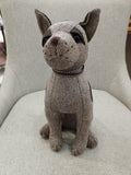 Estatueta de cão em tecido cinza com padrão espinha de peixe sentada numa cadeira cinza claro