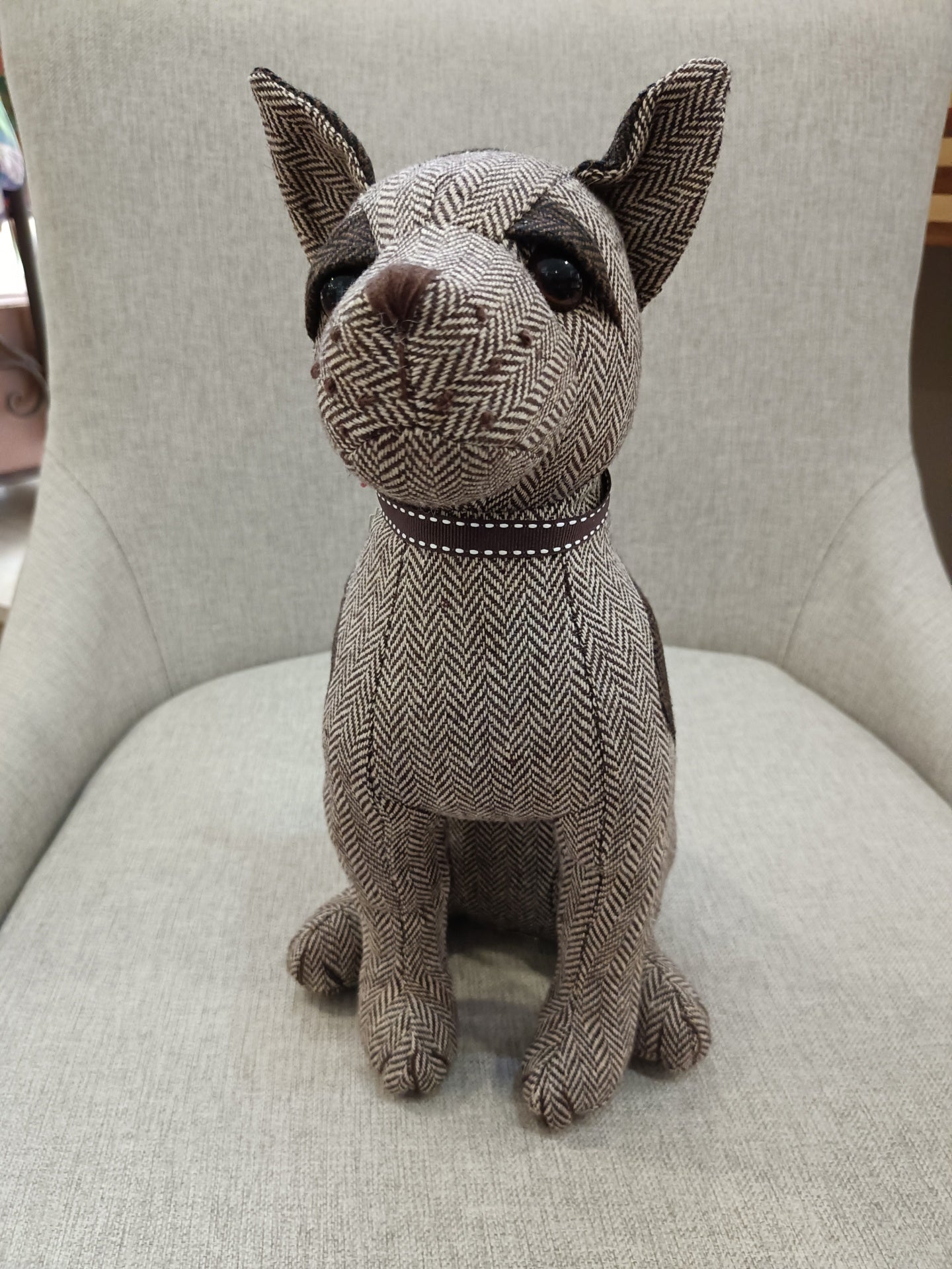 Estatueta de cão em tecido cinza com padrão espinha de peixe sentada numa cadeira cinza claro