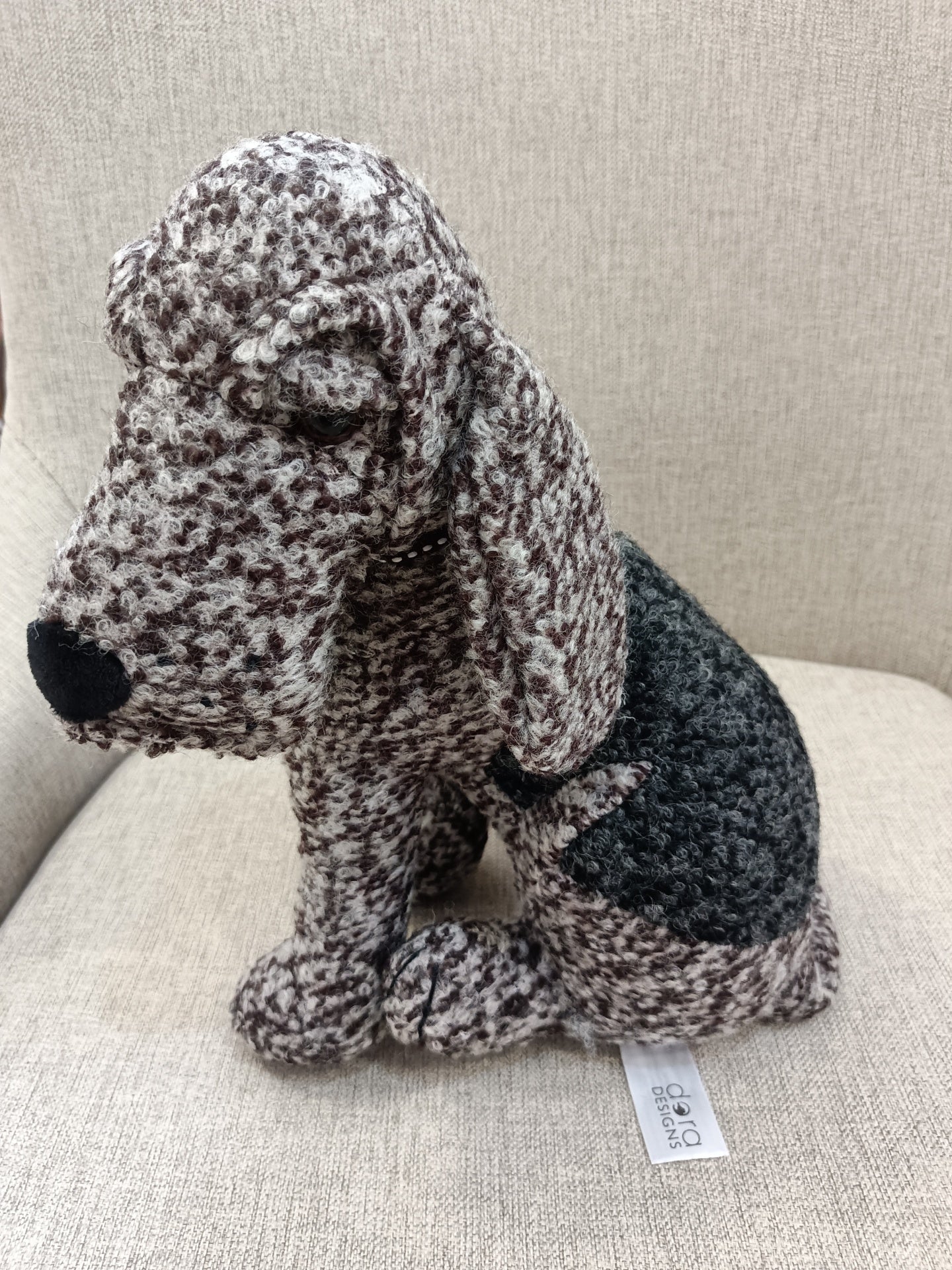 Estatueta de cão de tecido cinza e preto sobre sofá bege
