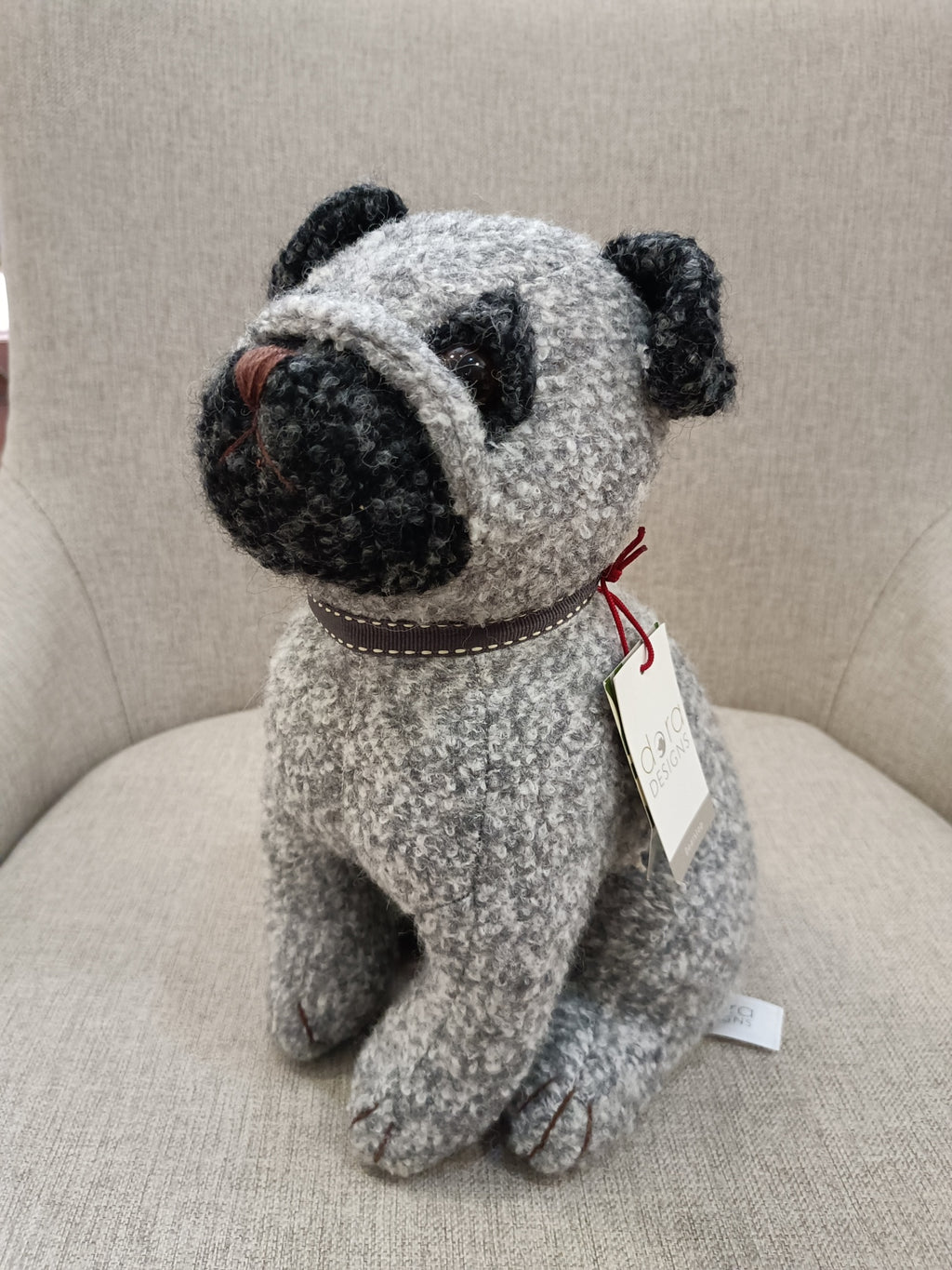 Boneco de cão cinza e preto sentado numa cadeira cinzenta clara