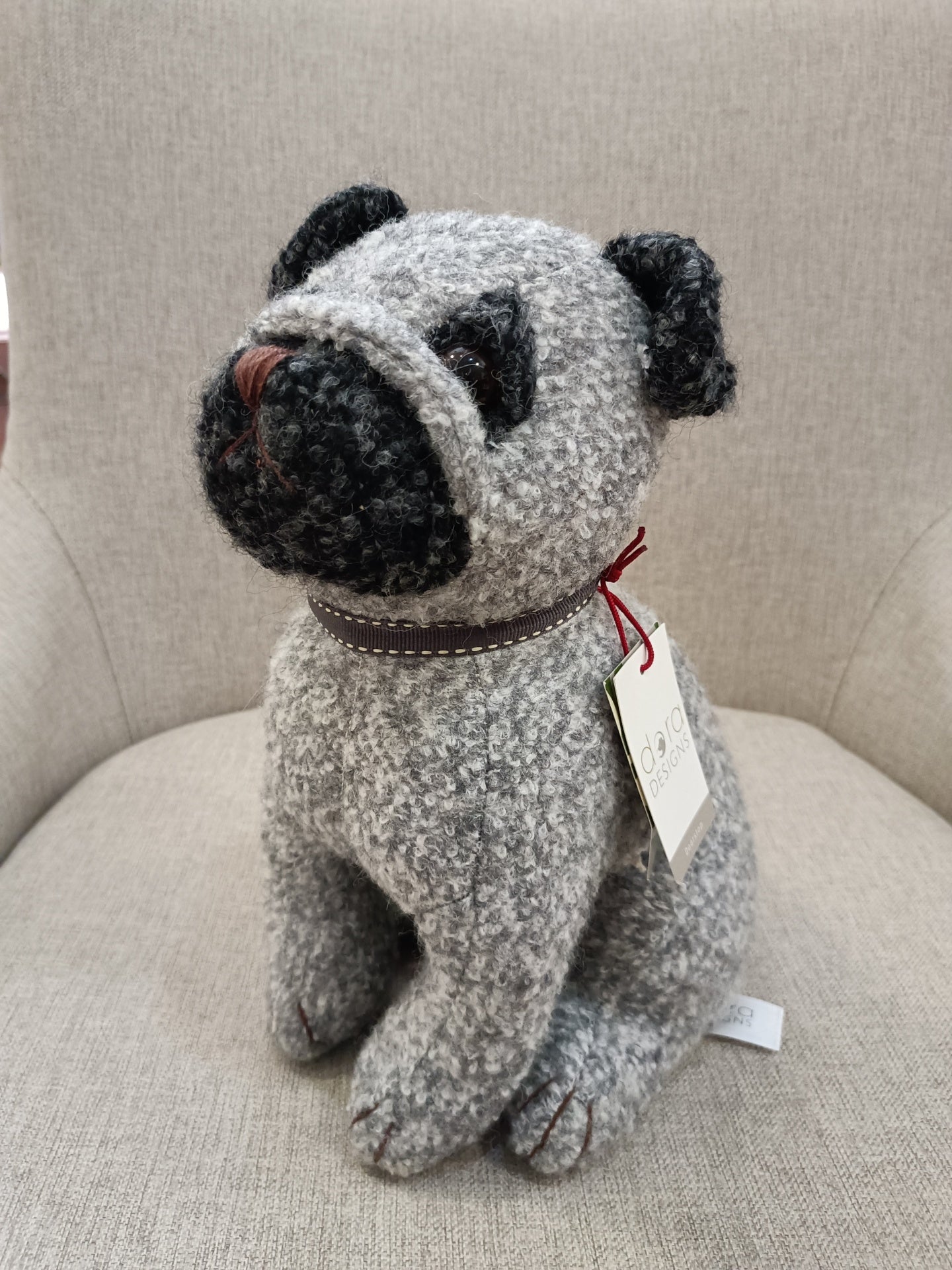 Boneco de cão cinza e preto sentado numa cadeira cinzenta clara