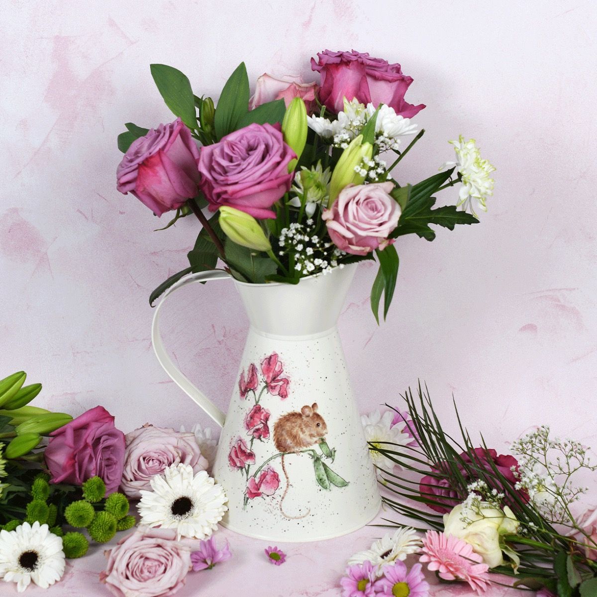 Jarro branco decorado com ratinho e flores, contendo arranjo floral em tons roxos, brancos e verdes