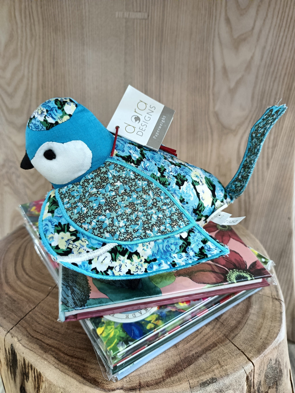 Pássaro de tecido azul decorativo com padrões florais sobre livros coloridos