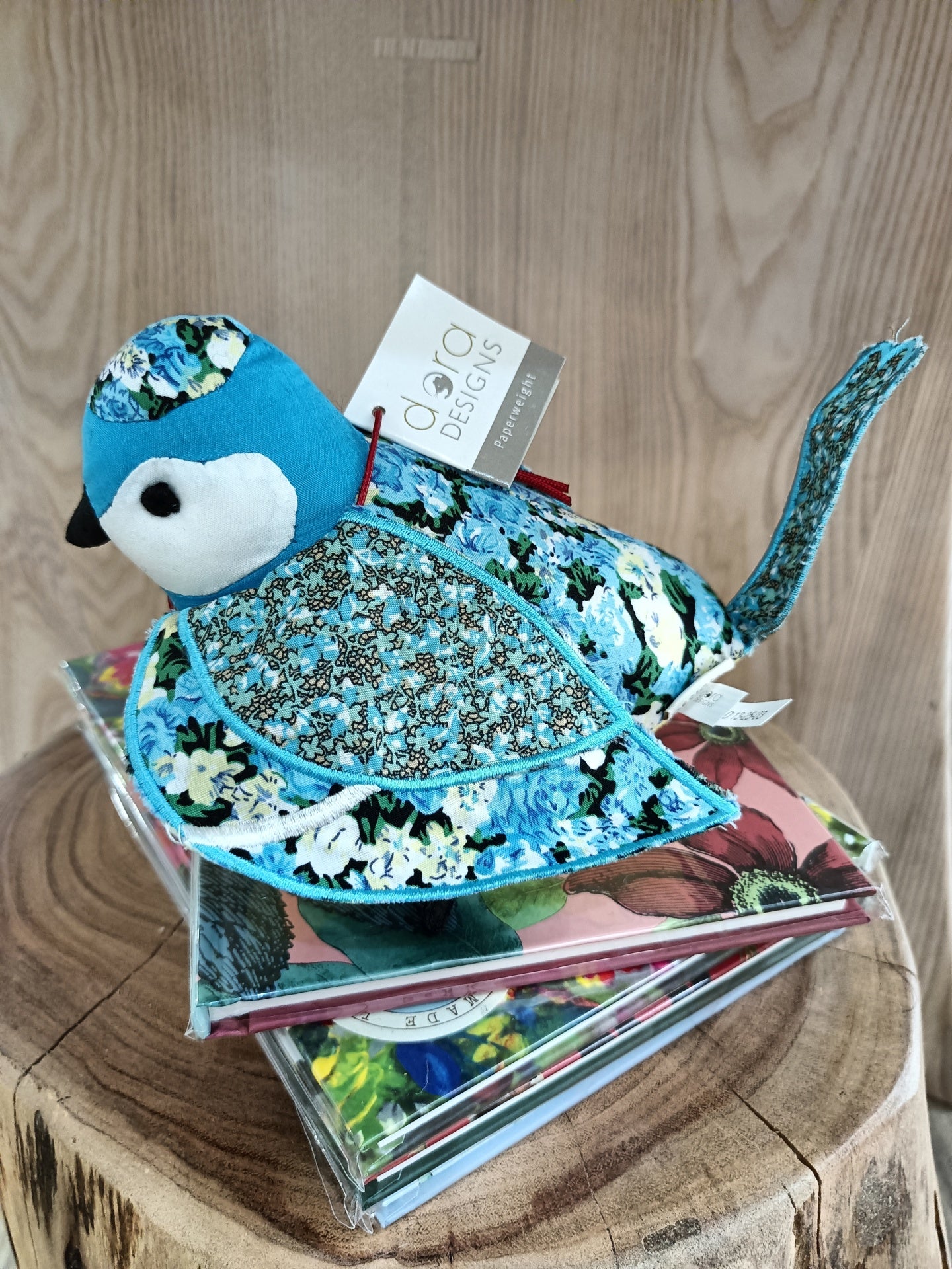 Pássaro de tecido azul decorativo com padrões florais sobre livros coloridos